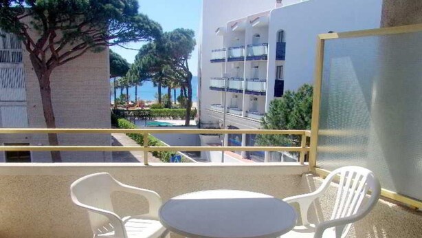 A balcony with a table and two chairs, overlooking a pool and buildings.