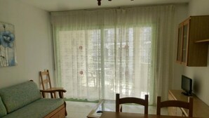 A living room with a sofa, a dining table, chairs, a TV, and a window with curtains.