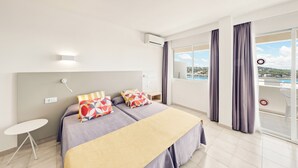 A modern hotel room with a bed, a small table, and a view of the city through large windows. - Vista Club Apartamentos (Calvia)