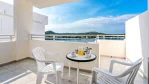 A balcony with white plastic chairs, a small round table with a coffee pot and cups, and a view of a body of water and hills in the distance. - Vista Club Apartamentos (Calvia)