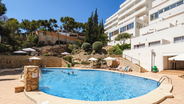 A swimming pool with a stone wall, lounge chairs, and umbrellas. - Vista Club Apartamentos (Calvia)
