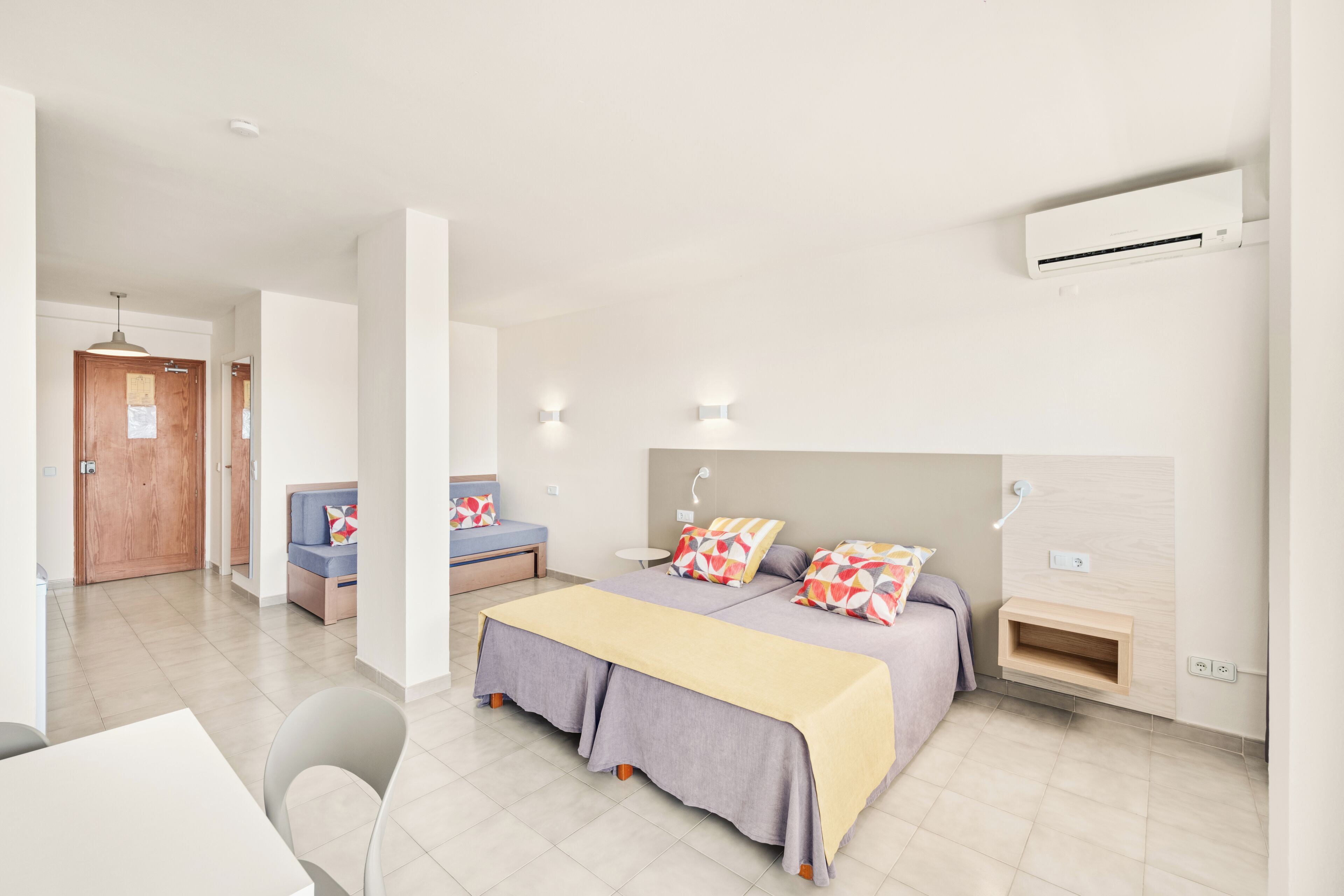 A modern hotel room with a bed, bedside tables, a desk, and a chair.