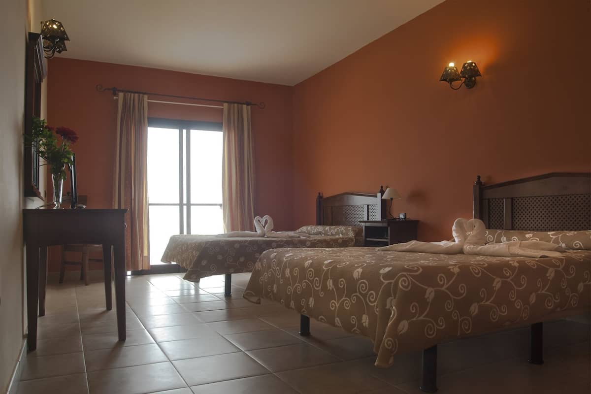 A hotel room with two beds, a desk, a chair, and a window with curtains.