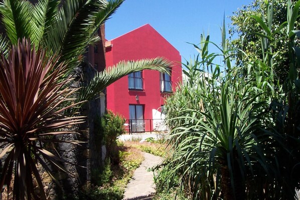 A red building with a pathway leading to the entrance, surrounded by greenery.