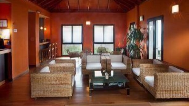 Un vestíbulo amplio con muebles de mimbre, una mesa de centro y ventanas grandes que dejan entrar luz natural.