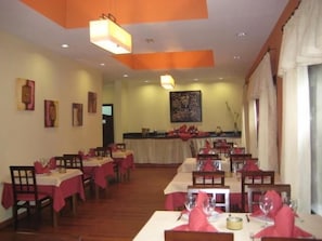 A restaurant with multiple tables set for dining, featuring red tablecloths and white napkins.