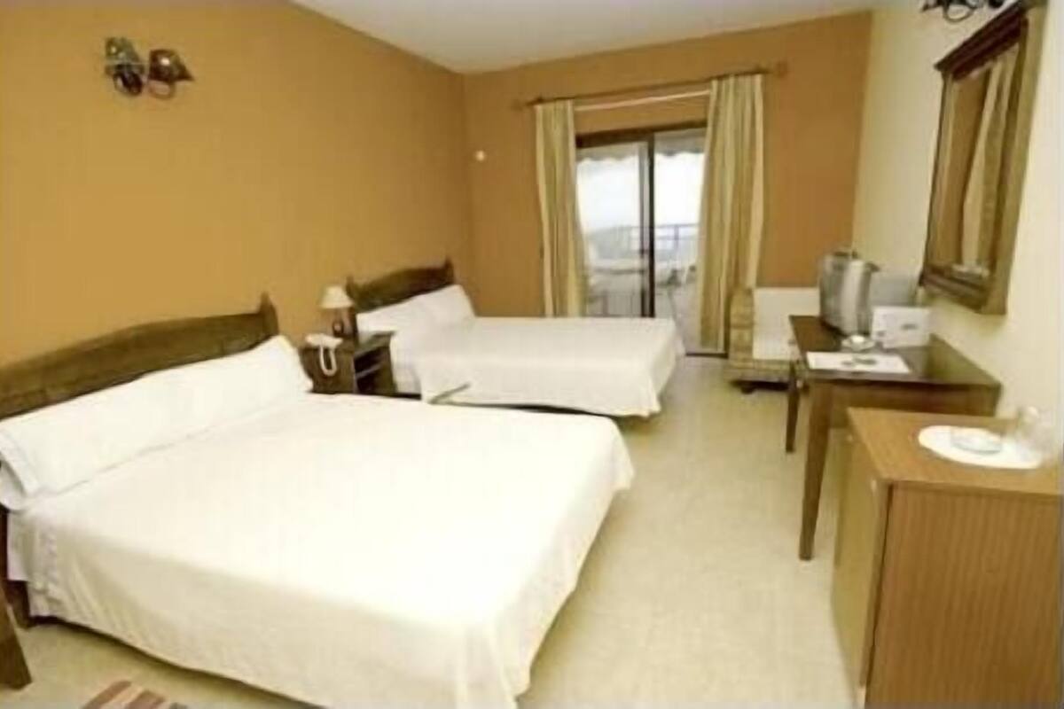 A hotel room with two beds, a desk, a chair, a TV, and a window with curtains.