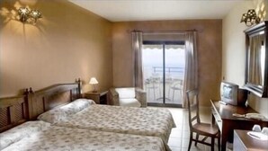 Habitación de hotel con dos camas, un escritorio, una silla, televisión y un balcón con vistas.