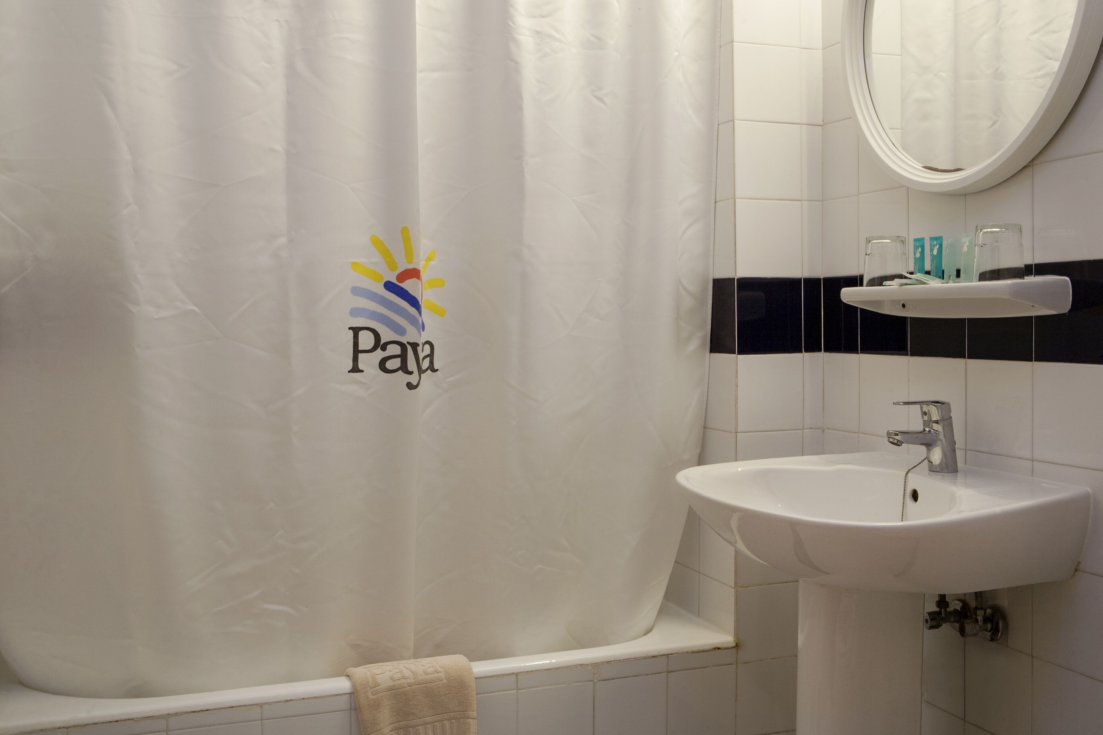 A bathroom with a white sink, a mirror, and a shower curtain with a logo.