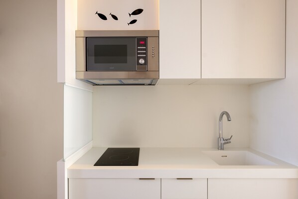 Een kleine keuken met een inbouwmagnetron, een spoelbak en een roestvrijstalen kraan.