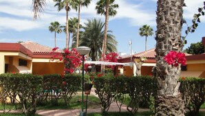 Une cour d’hôtel agrémentée de palmiers, de fleurs rouges et surmontée d’un toit en tuiles.