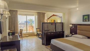 A hotel room with a bed, a desk with a lamp, a chair, a view of the outside, and a decorative partition.