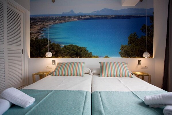 A double bed with striped pillows and a view of a coastal landscape.