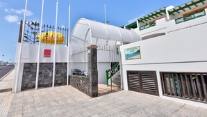A building entrance with a white facade, a stone wall, and a metal gate. - Apartamentos Isabel (Tias)