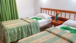 A room with two single beds, each with a green floral bedspread and white pillows. There is a wooden nightstand with a vase of flowers between the beds. - Apartamentos Isabel (Tias)