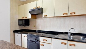 A compact kitchen with light wood cabinets, a black microwave, and a stainless steel sink. - Apartamentos Isabel (Tias)