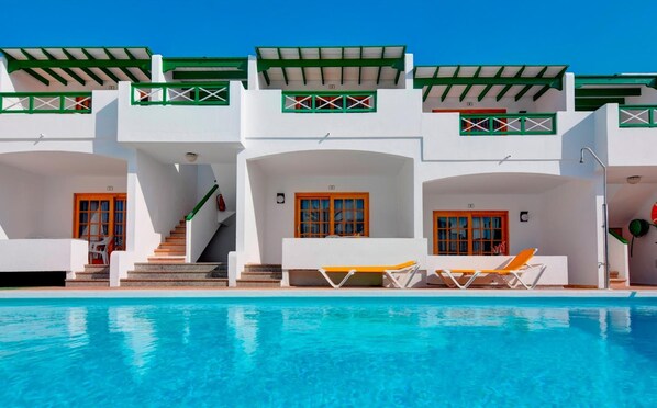 A modern hotel with a pool, featuring multiple balconies, a staircase, and lounge chairs. - Apartamentos Isabel (Tias)