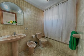 A bathroom with a sink, bidet, toilet, and a shower curtain. - Apartamentos Isabel (Tias)