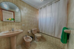 A bathroom with a sink, bidet, toilet, and a shower curtain. - Apartamentos Isabel (Tias)