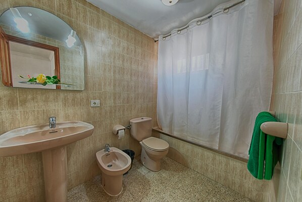 A bathroom with a sink, bidet, toilet, and a shower curtain. - Apartamentos Isabel (Tias)