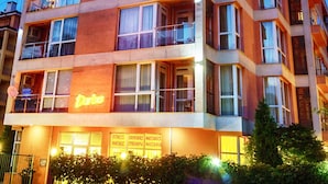 A multi-story hotel with balconies, large windows, and a neon sign indicating it offers fitness, souvenirs, and massages. - Darius (Sunny Beach)