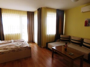 A hotel room with a bed, a sofa, a coffee table, and a window with curtains. - Darius (Sunny Beach)