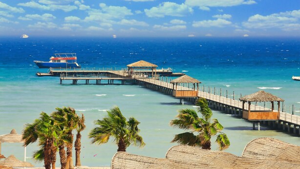 A pier extending into a clear blue sea with a boat docked at the end. - Amwaj Beach Club Abu Soma - All inclusive (Safaga)