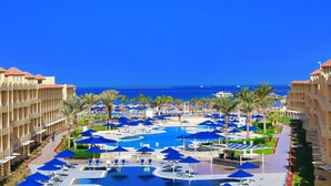 A resort with a central pool surrounded by lounge chairs and umbrellas, a clear view of the ocean, and a multi-story building with balconies. - Amwaj Beach Club Abu Soma - All inclusive (Safaga)