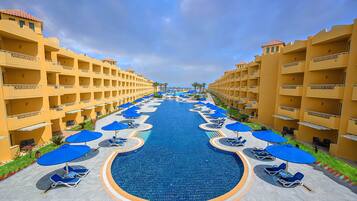 A hotel with a central swimming pool, multiple balconies, and sun loungers with umbrellas.