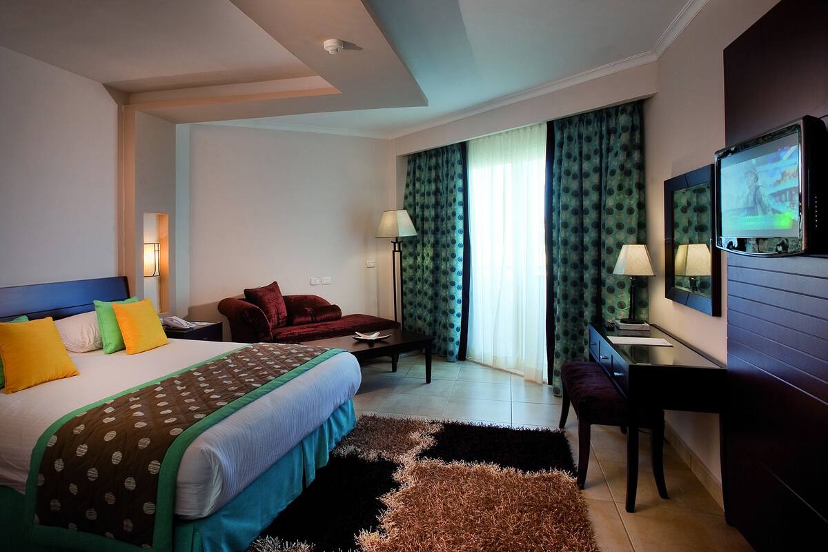 A hotel room with a bed, a desk, a chair, a TV, and a window with curtains.