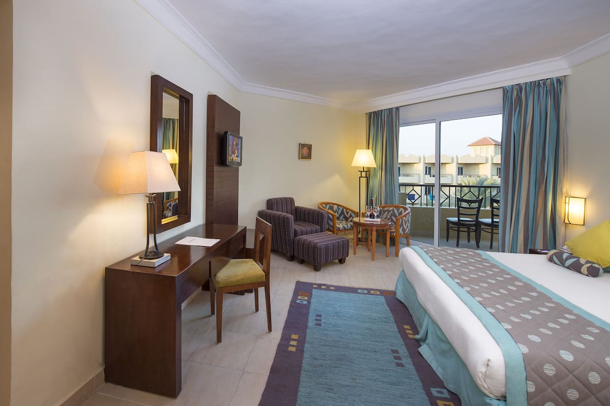 A hotel room with a bed, bedside tables, a desk, a chair, and a balcony with curtains.