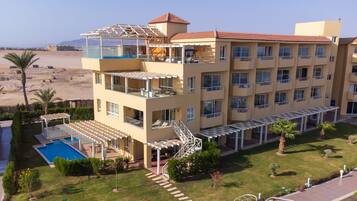 A multi-story hotel with balconies, a pool, and a view of the beach.