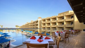 A poolside dining area with tables set for guests, overlooking a pool with umbrellas and lounge chairs. - Amwaj Beach Club Abu Soma - All inclusive (Safaga)