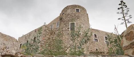 An ancient stone building with a round tower, narrow windows, and overgrown vegetation.