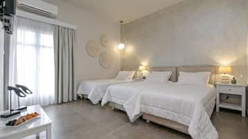 A hotel room with two beds, a desk with a plate of fruit, and a wall-mounted air conditioner.