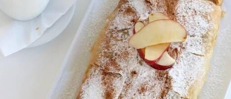 A rectangular pastry with powdered sugar and apple slices on top, being cut with a knife.