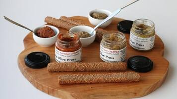 A wooden board with jars of olive press condiments and two wooden sticks.