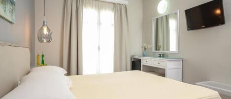 Habitación de hotel con cama, escritorio, silla, televisión y ventana con cortinas.