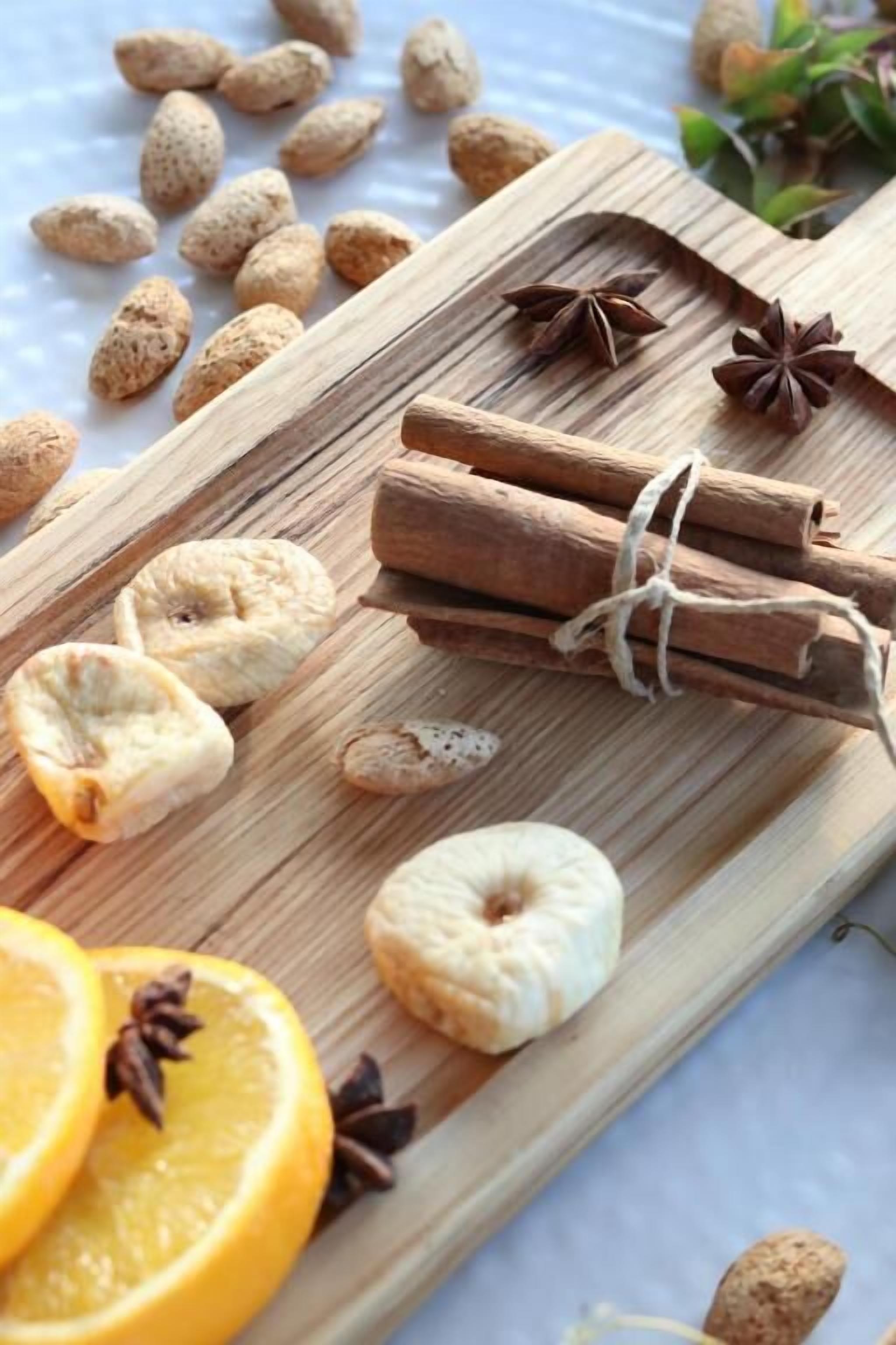 Een houten snijplank met schijfjes sinaasappel, kaneelstokjes, steranijs en amandelen.
