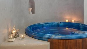 A spa room with a wooden floor, a blue hot tub, candles, and a small window. - Grotta Hotel (Naxos)