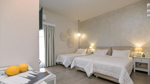 A hotel room with two beds, a small table with a magazine and lemons, and a window with curtains. - Grotta Hotel (Naxos)
