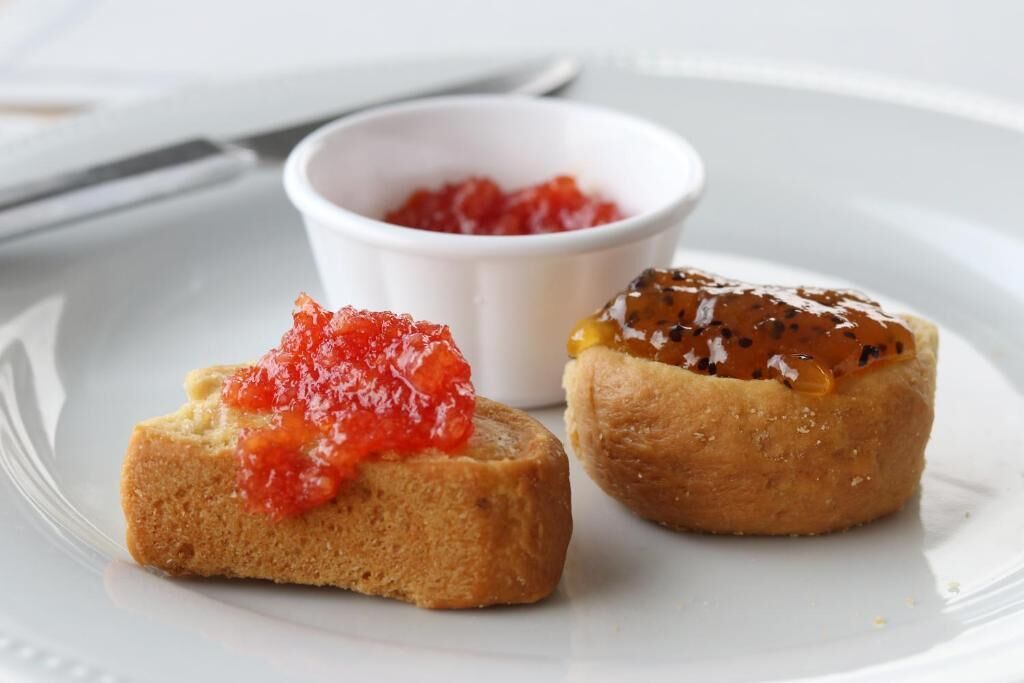 Two small sandwiches on a white plate, one with red spread and the other with a brown sauce.