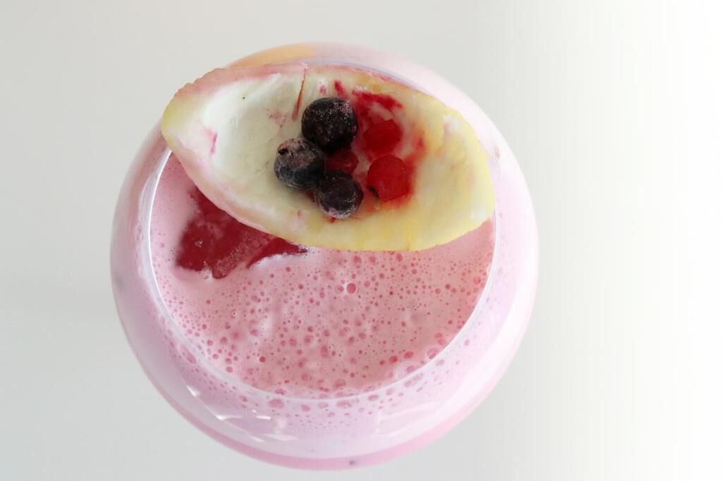 A pink beverage with a slice of fruit and berries on top.