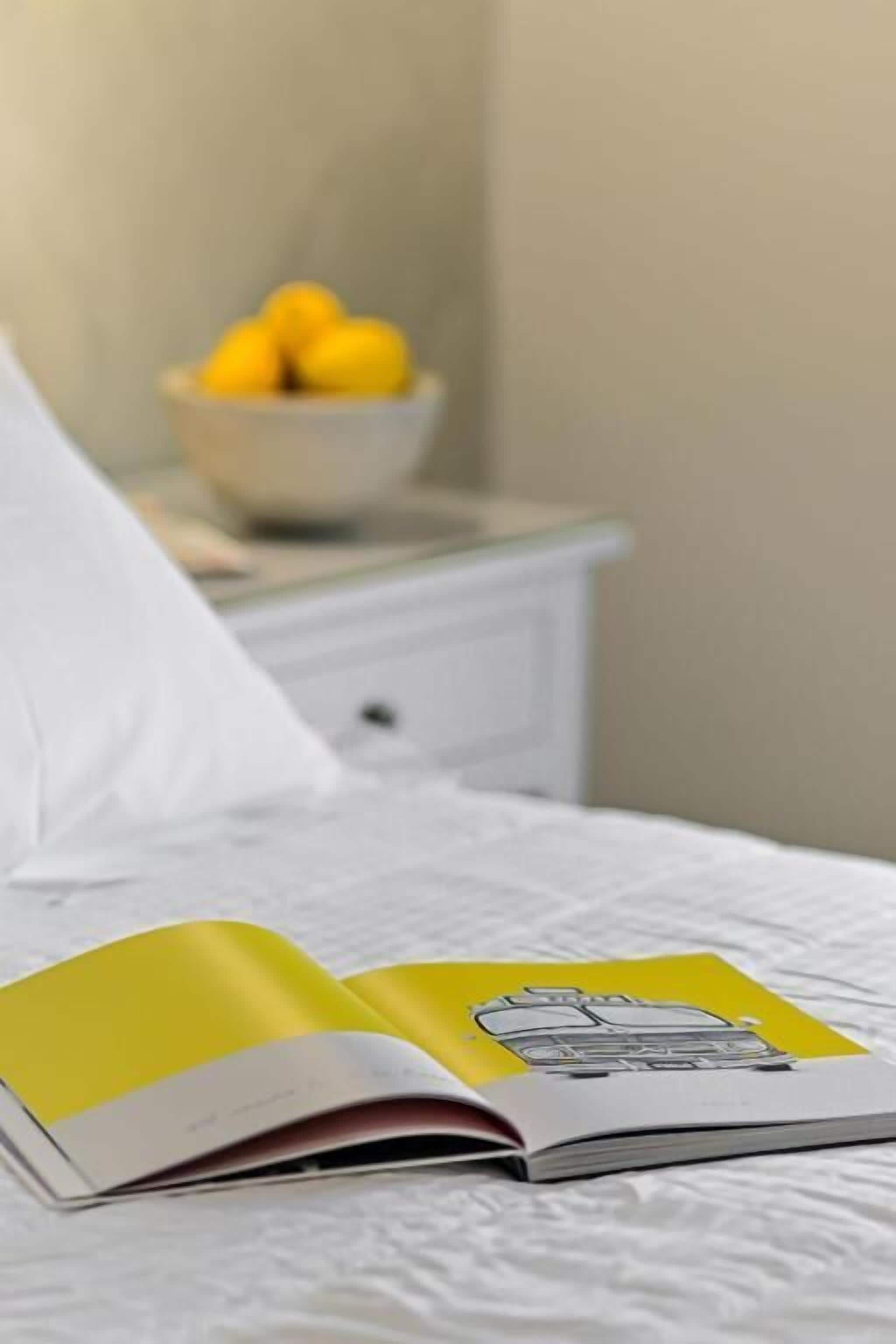 A bed with a white sheet and a book open on it.