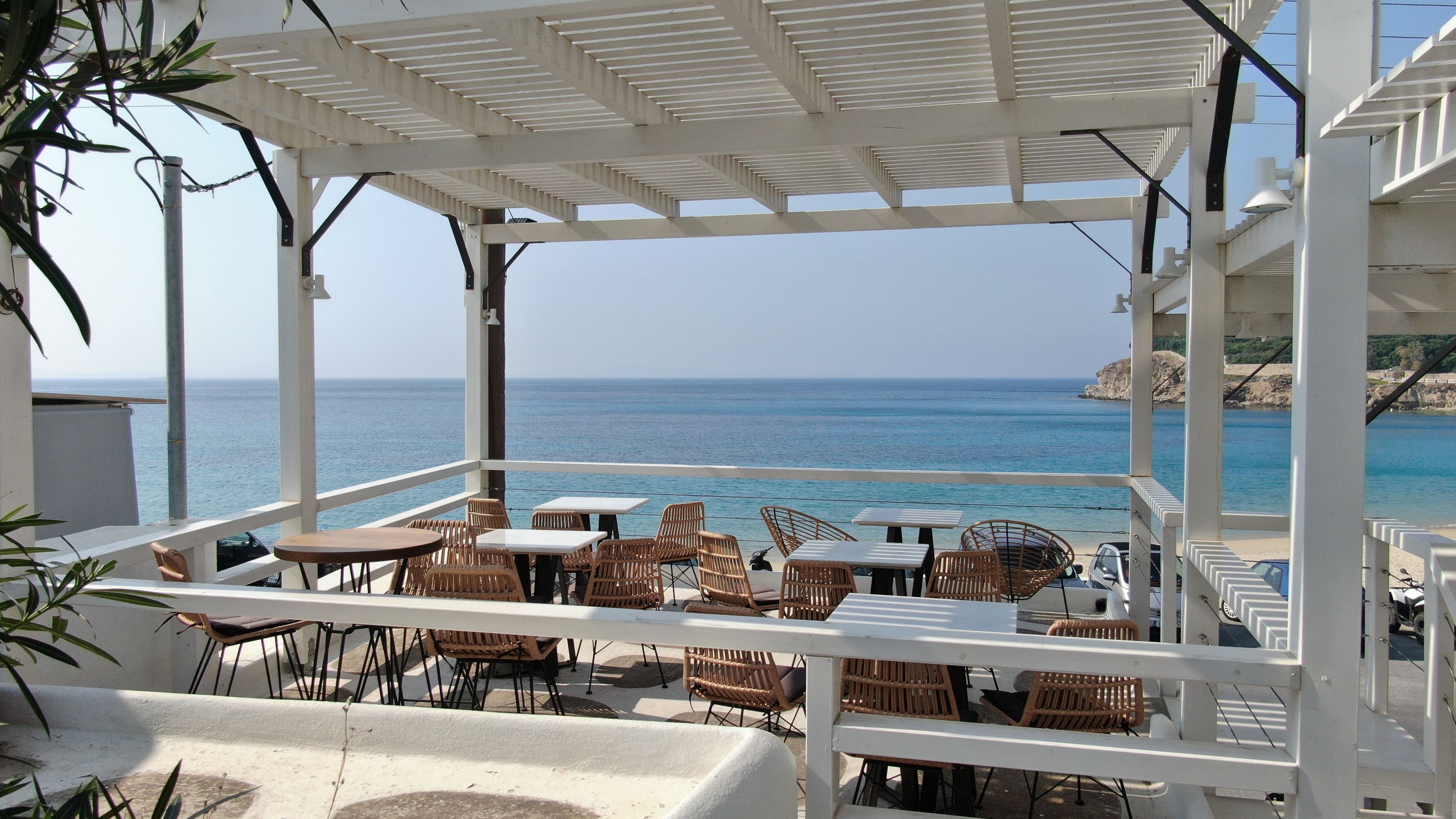 An outdoor seating area with tables and wicker chairs, overlooking a body of water.