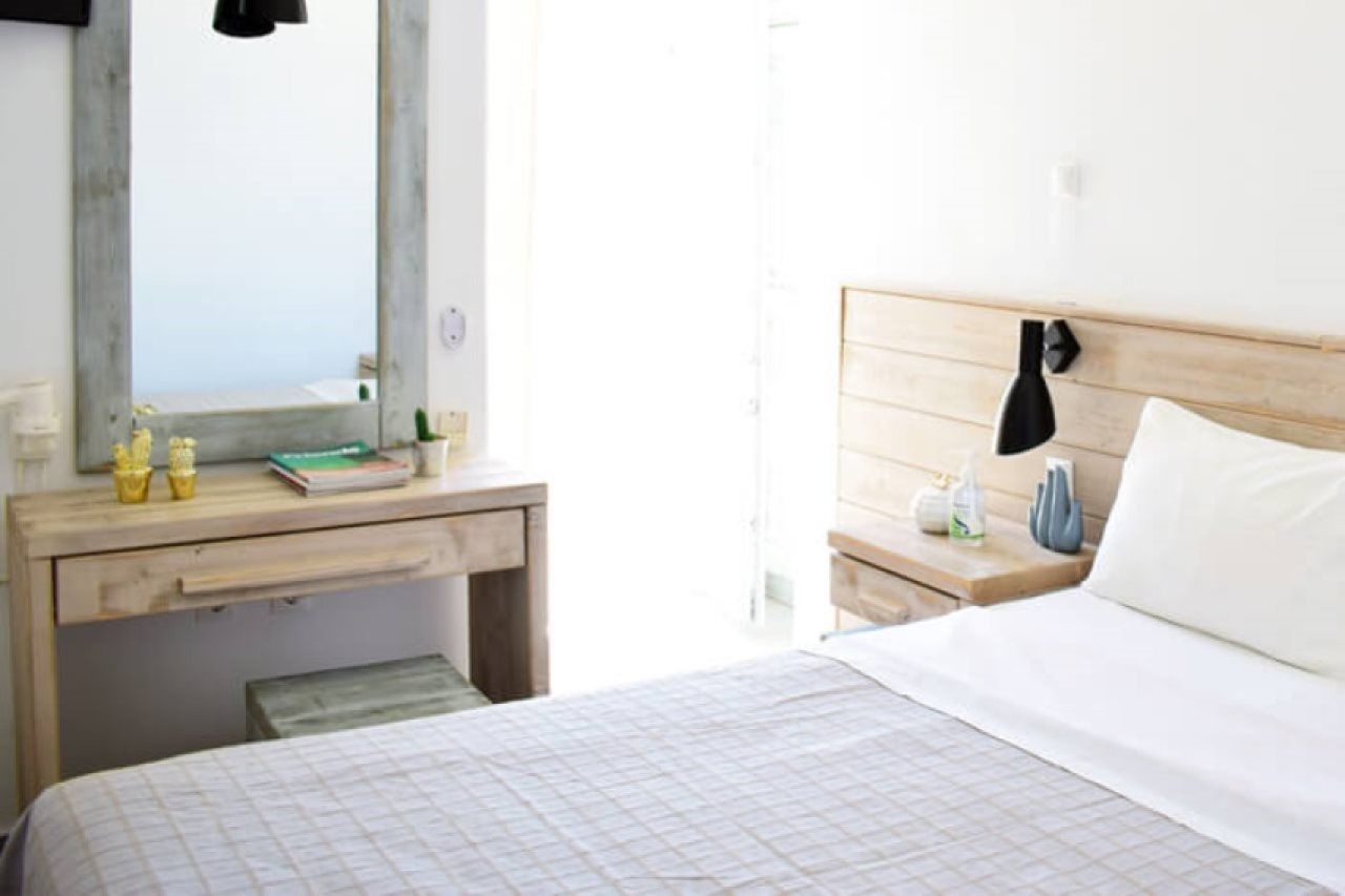 A bedroom with a bed, a wooden nightstand, a mirror, and a window.