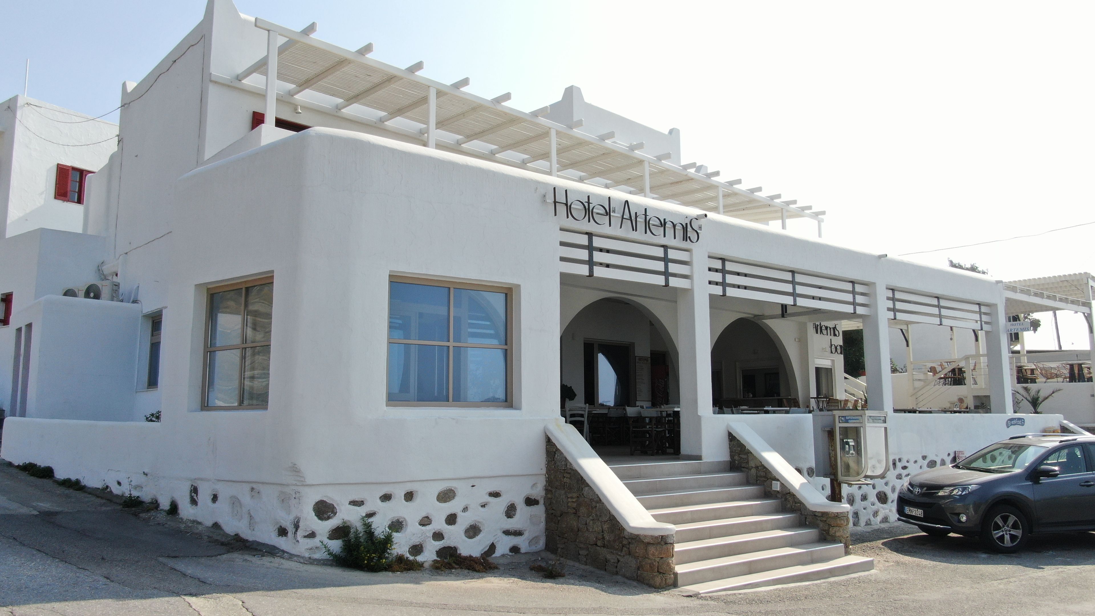 Un edificio blanco con un letrero que dice 'Hotel Artemis'. Tiene una entrada cubierta con escalones que conducen a ella.
