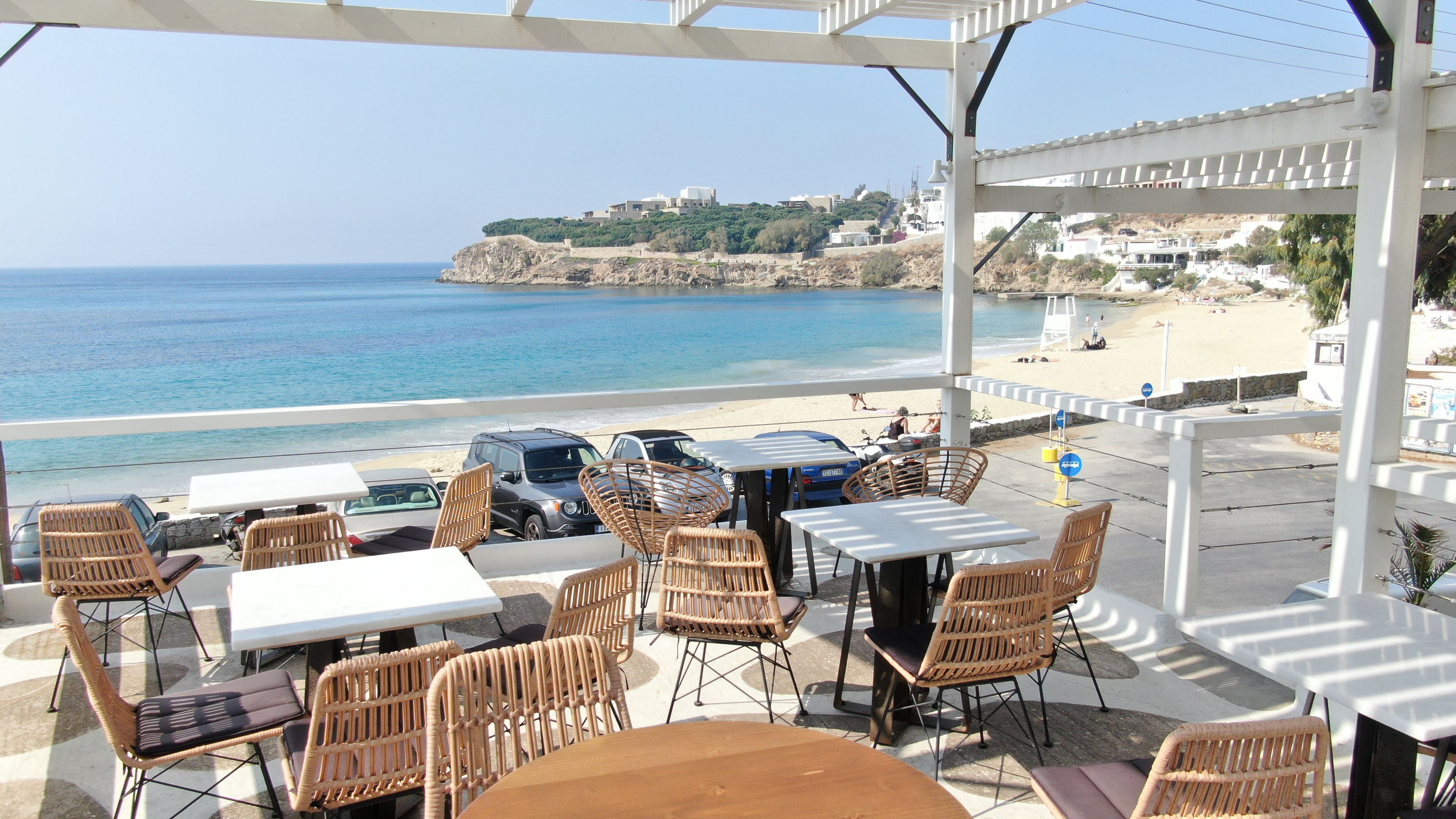 An outdoor seating area with tables and chairs overlooking a beach and the sea.