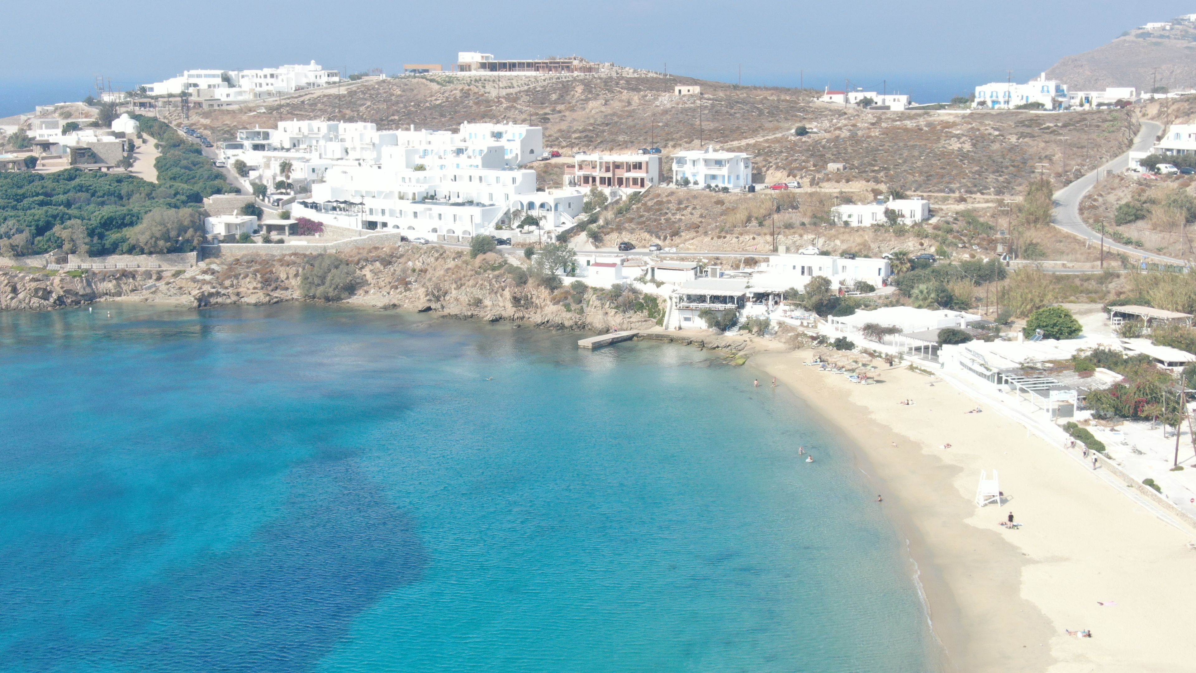 A coastal town with white buildings, a beach, and clear blue waters.