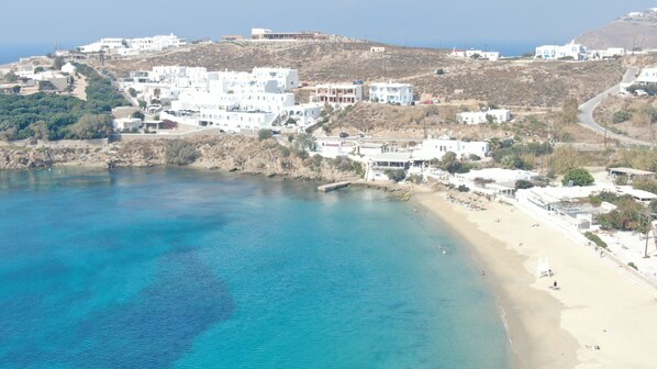 A coastal town with white buildings, a beach, and clear blue waters. - Artemis (Mykonos)